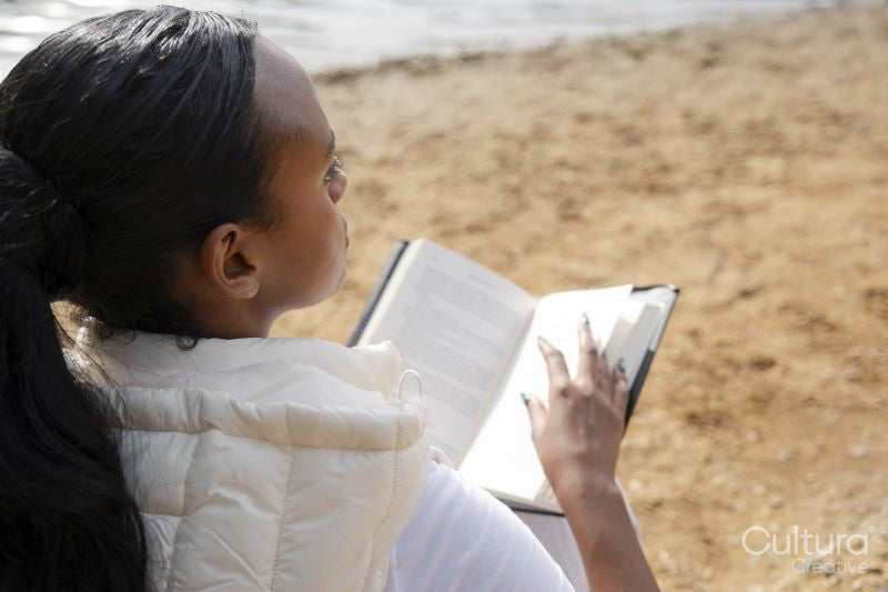 Rear view of woman reading book on lakeshore