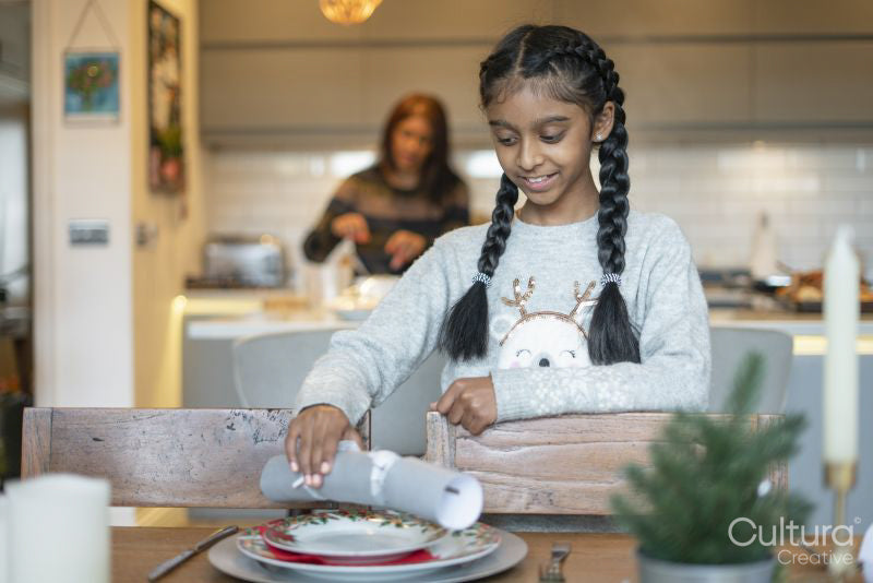 Smiling girl placing Christmas cracker on table, mother in background