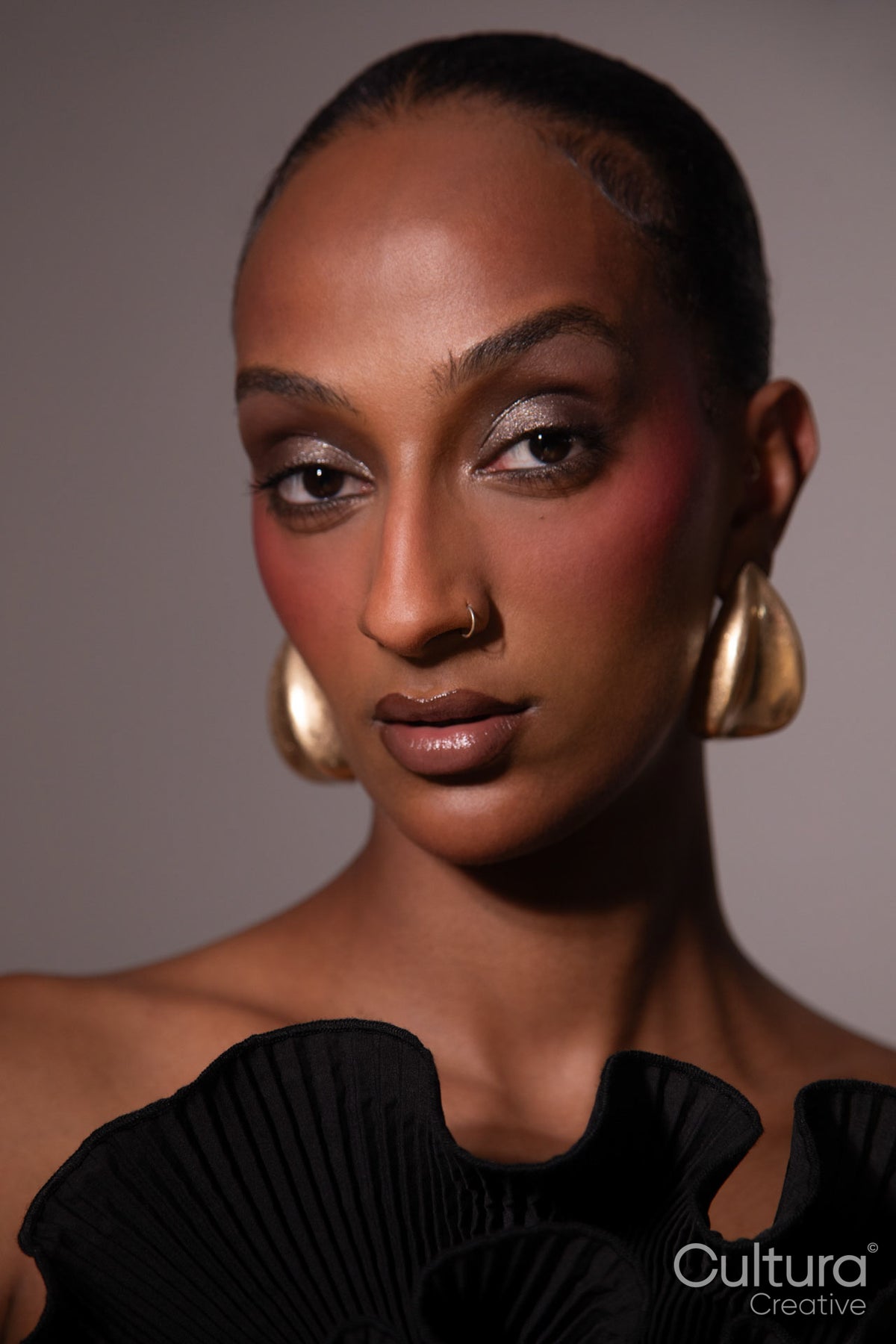 Woman in a black dress with gold earrings on a grey background