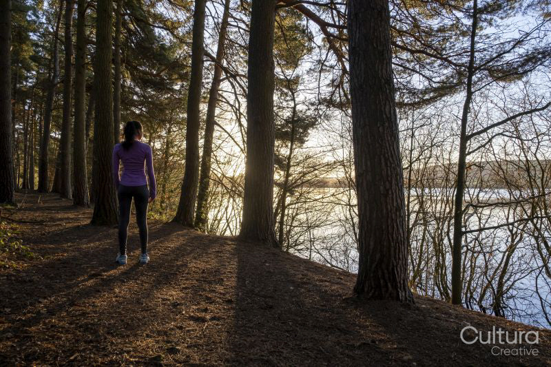 Female jogger standing in forest and looking at lake