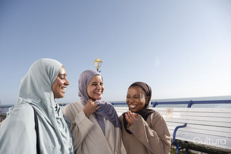 Three Muslim women laughing while standing on pier on sunny day
