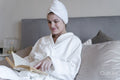 Woman in bathrobe reading book on bed