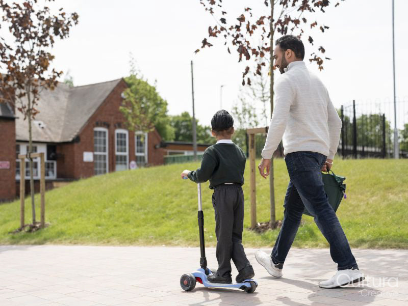 Boy on push scooter walking with father to school