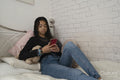 Teenage girl using smart phone while relaxing on bed at home