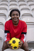 Portrait of smiling athletic woman sitting on chair at stadium with soccer ball