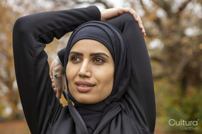 Close-up of woman in black sports clothing and hijab stretching in park