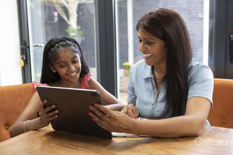 Smiling mother and daughter using digital tablet at home