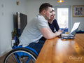 Man on wheelchair and woman looking at laptop at home