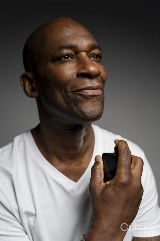 Portrait of man putting on perfume against gray background