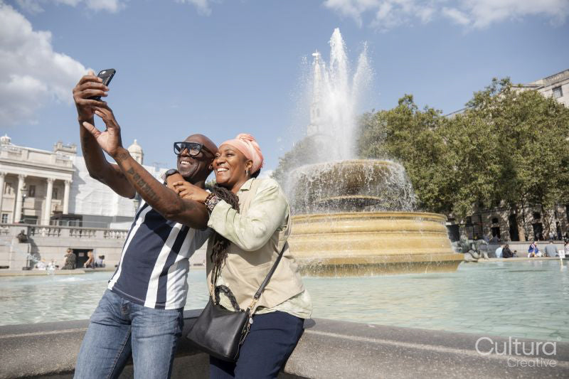 Happy mature couple taking selfie next to fountain in Trafalgar Square