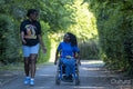 Teenage girl in wheelchair with friend walking in park