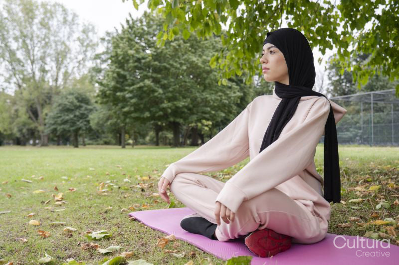 Woman in hijab and pink tracksuit meditating in park