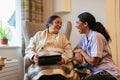 Senior lady sitting in armchair and showing tablet to nurse at nursing home