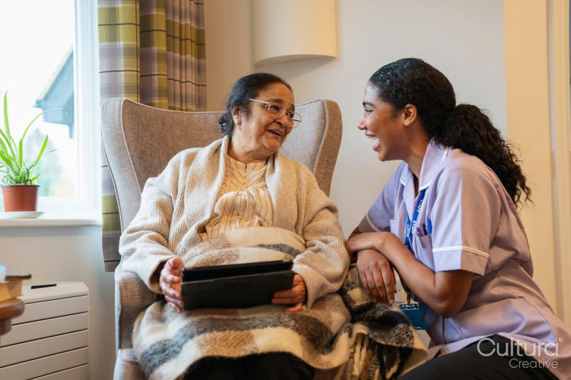 Senior lady sitting in armchair and showing tablet to nurse at nursing home
