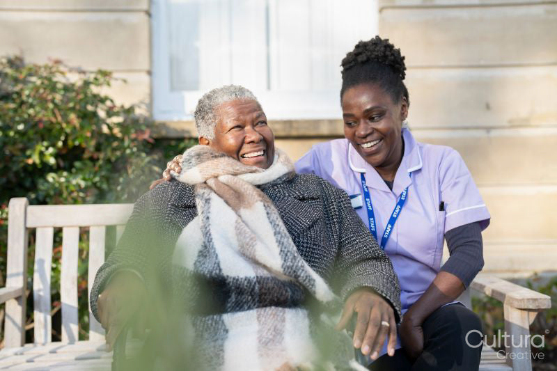 Smiling nurse and senior woman in wheelchair relaxing in park
