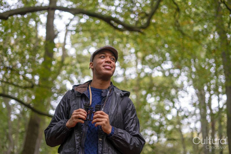 Man looking up and holding binoculars in forest