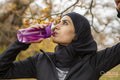 Woman in black sports clothing and hijab drinking water in park