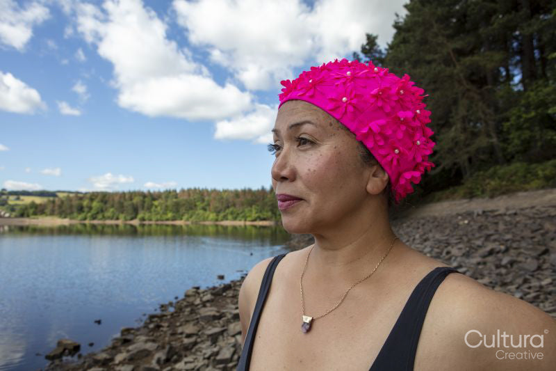 Woman in pink swimming cap standing on rocky lakeshore, Yorkshire, UK