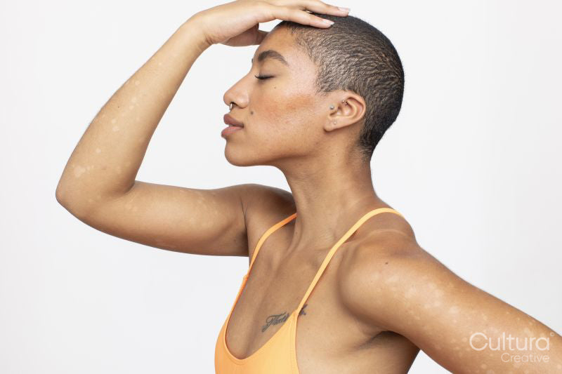 Profile of woman wearing orange top touching head