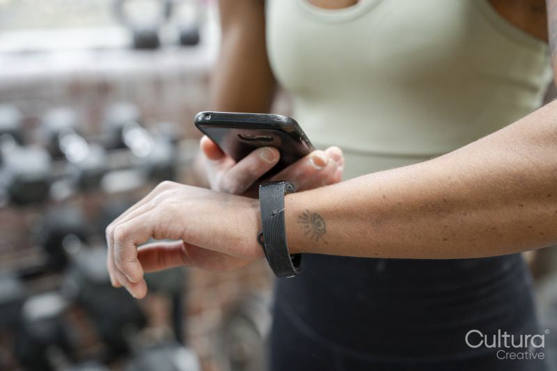 Woman using smart phone and fitness tracker on gym
