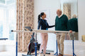 Female therapist assisting senior man walking on bars in exercise room