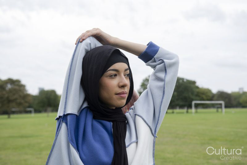 Portrait of woman in hijab stretching arm in park