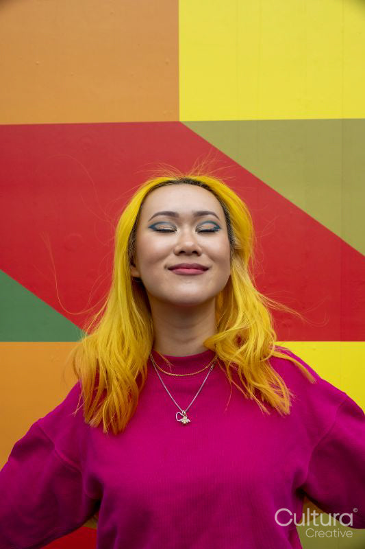 Smiling young woman with yellow hair against colorful wall