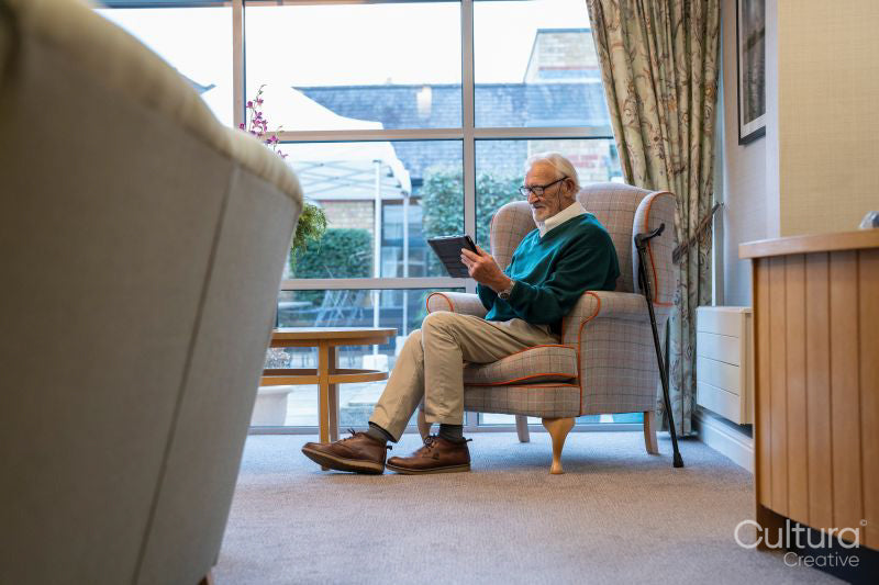 Senior man sitting in armchair and using tablet in nursing home