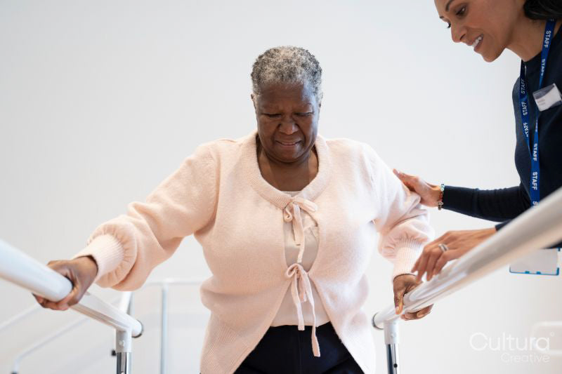 Female therapist assisting senior woman walking on bars in exercise room
