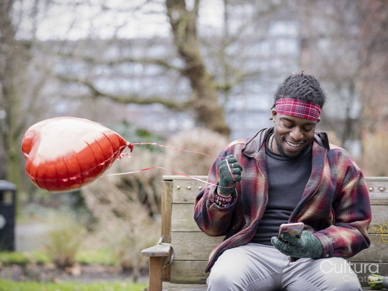 Smiling man with heart shaped balloon sitting on bench