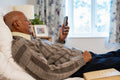 Senior man during video call on phone while lying on bed in his room at nursing home