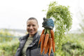 Portrait of smiling woman holding bunch of carrots in urban garden
