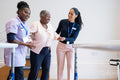 Female therapist and nurse supporting senior woman walking in exercise room