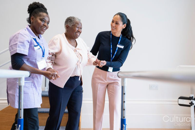 Female therapist and nurse supporting senior woman walking in exercise room