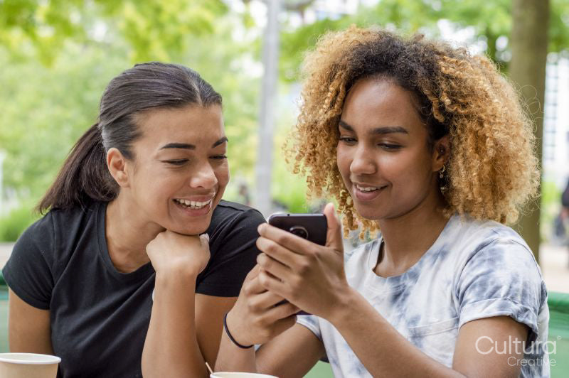 Two women using smart phone together while sitting in cafe