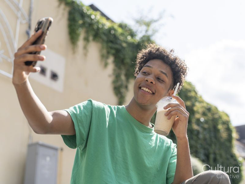 Young man taking selfie with smoothie on sunny day