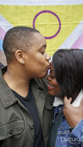 Two women kissing in front of pride flag