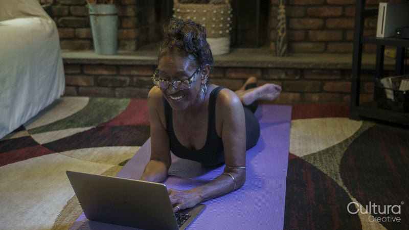 Senior woman lying on yoga mat and using laptop