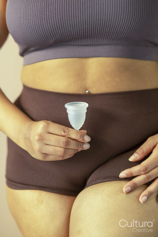 Mid section of woman in lingerie holding menstrual cup in front of belly
