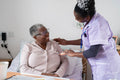 Caregiver assisting smiling senior woman sitting on bed