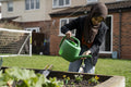 Woman wearing hijab watering flowers in backyard