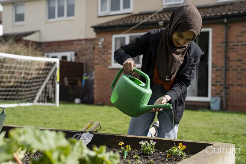 Woman wearing hijab watering flowers in backyard