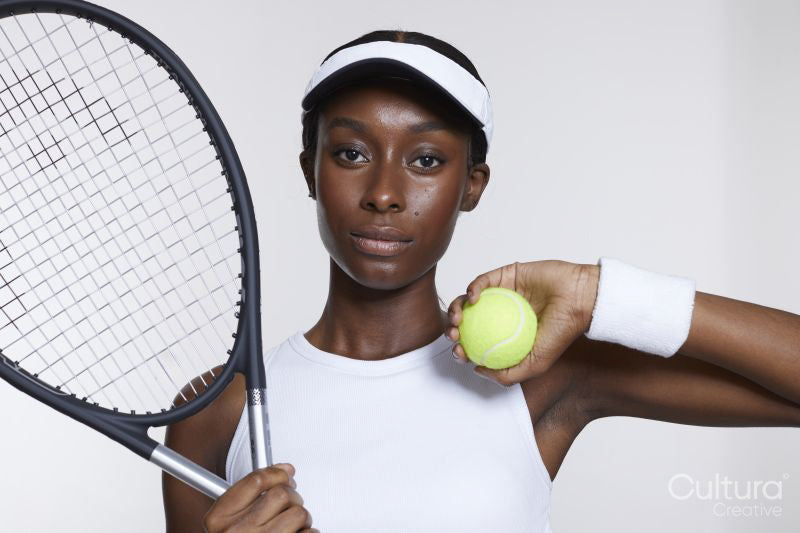 Studio portrait of athletic woman with tennis racket and ball