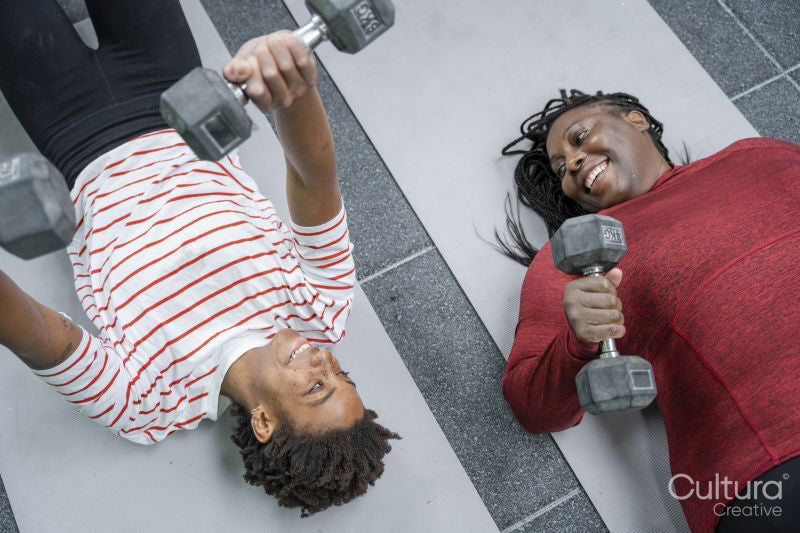 Mother and daughter doing weight training with dumbbells on mat in gym
