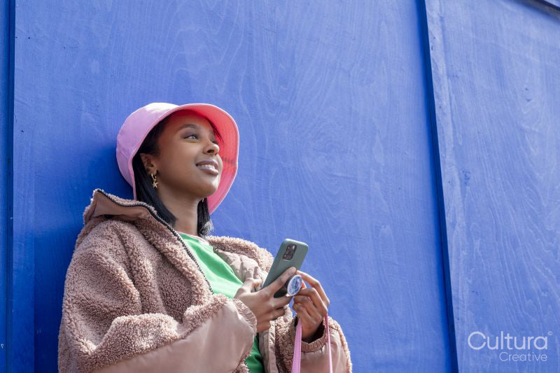Smiling young woman in bucket hat using phone outdoors