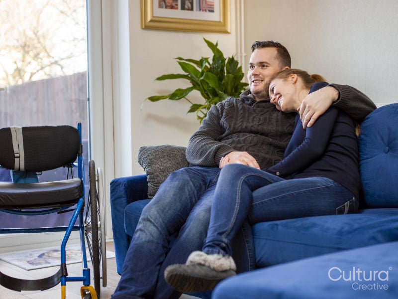 Smiling couple sitting on sofa next to wheelchair