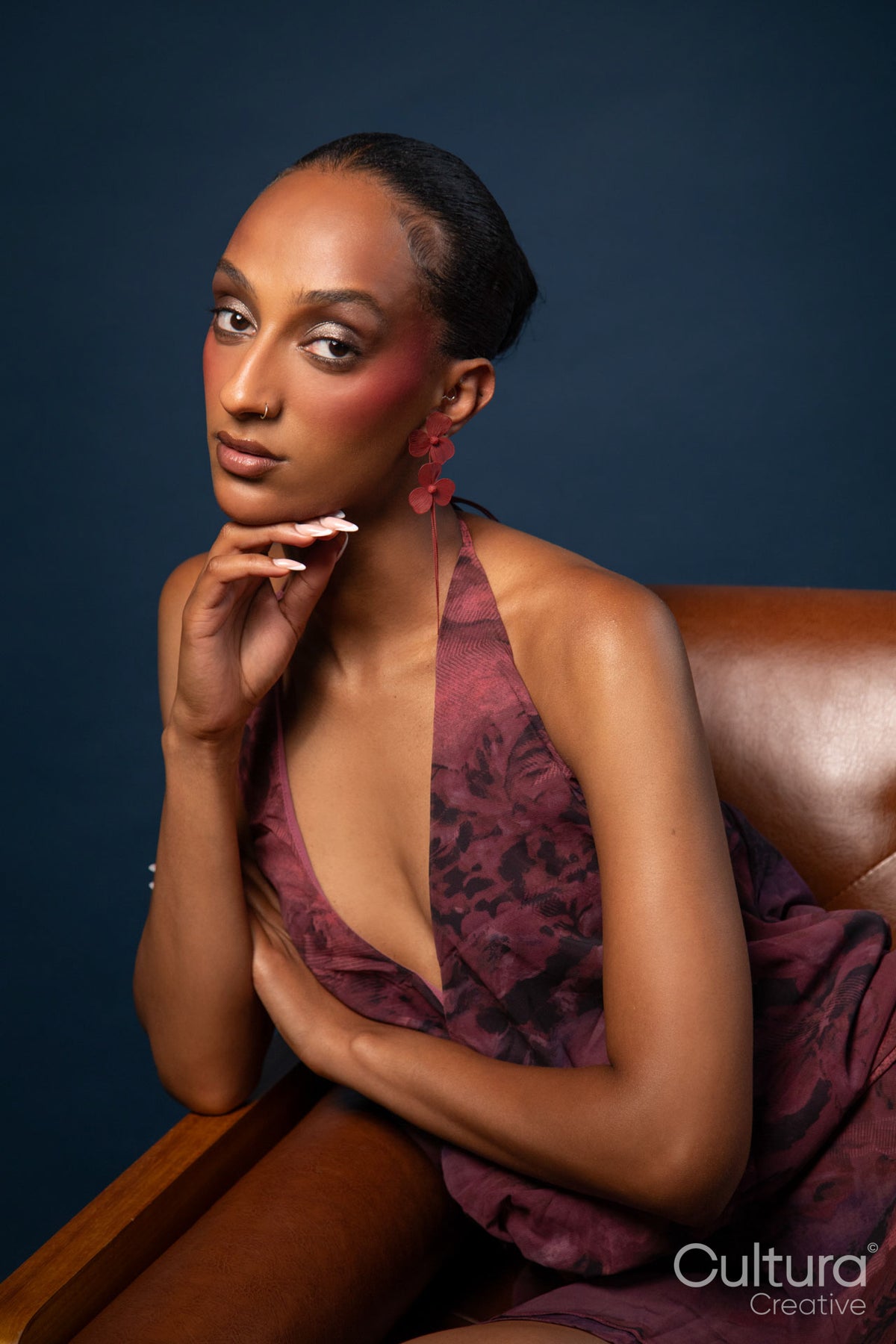 Woman in a burgundy dress with red earrings on a blue background