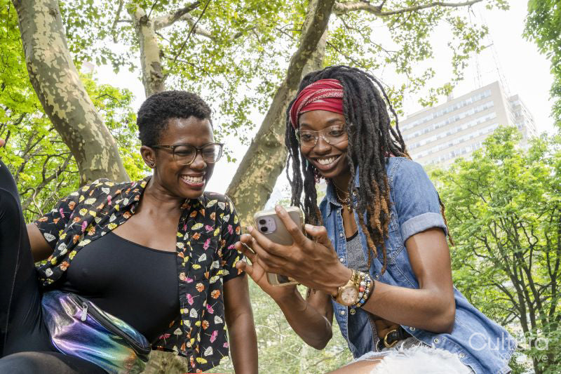 Two smiling young women looking at smart phone in park