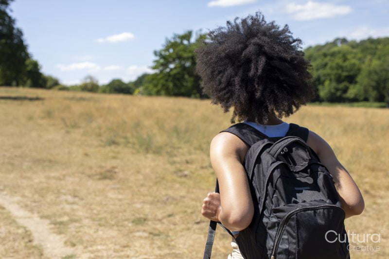 Young woman with backpack hiking in countryside, rear view