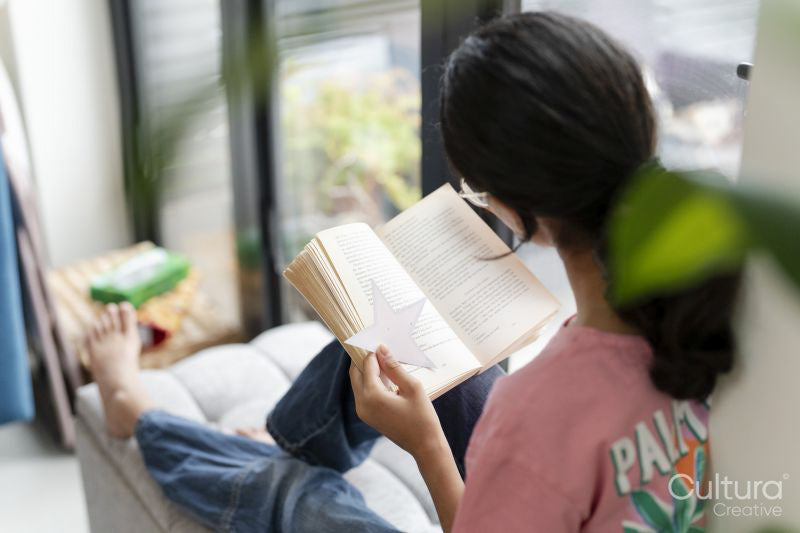 Girl sitting at hassock near window and reading book